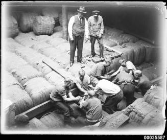 Cargo hold in MAGDALENE VINNEN with crew men securing wool bales