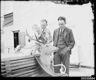 Two men and a child looking at a mounted deer head on board SS ORUNGAL