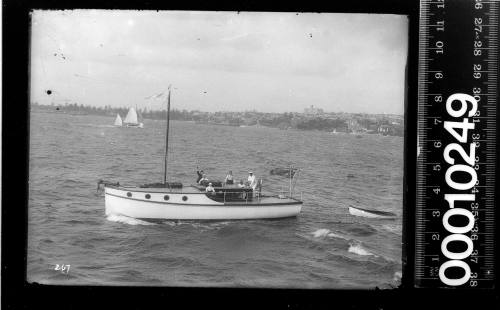 Raised deck motor launch towing a dinghy and flying an Australian flag from the stern, Sydney Harbour