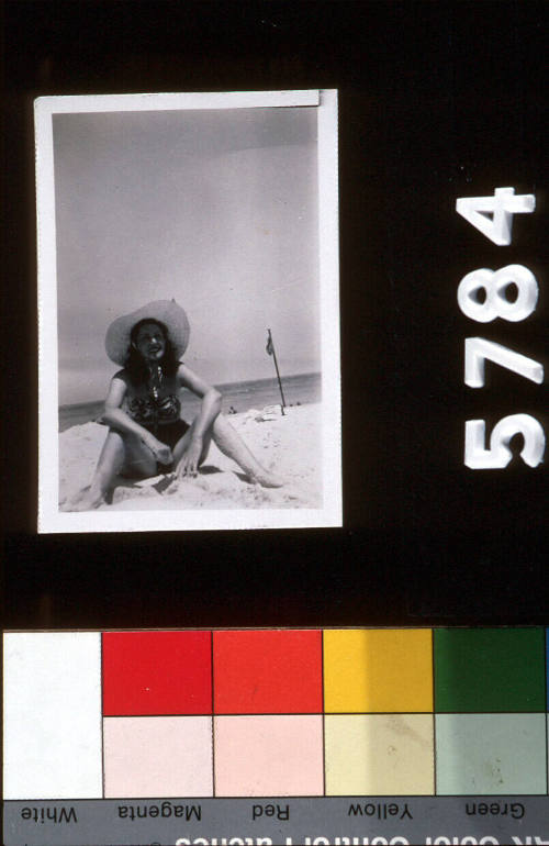 Beach holiday, woman in a swimsuit and sunhat sitting on the beach