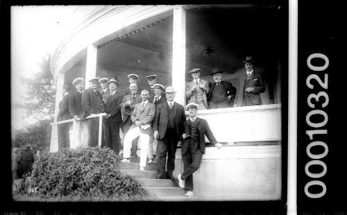 Men in yachting uniforms standing on the verandah of an unidentified yacht club