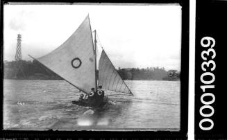 10-footer on Sydney Harbour displaying a circular emblem on the mainsail and the crew's shirts