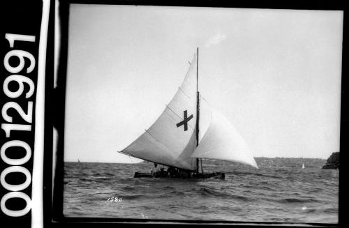 Yacht sailing near South Head, Sydney Harbour, with a large cross emblem displayed on the mainsail