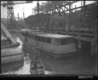 Image of a working wharf with men in suits preparing a small vessel for hoisting.