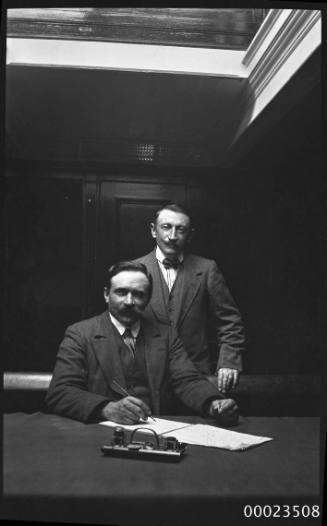 Portrait of two men in suits behind a table