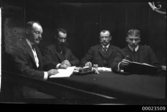 Four men wearing suits and seated around a table