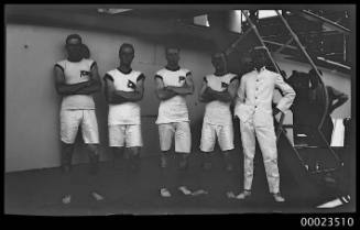 Four men in sports uniforms standing arms crossed with an officer