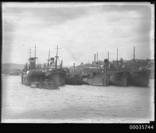 View of six ships berthed alongside wharves.