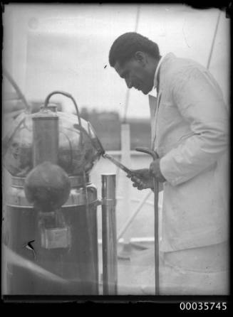 Man standing near binnacle and compass from unknown vessel.