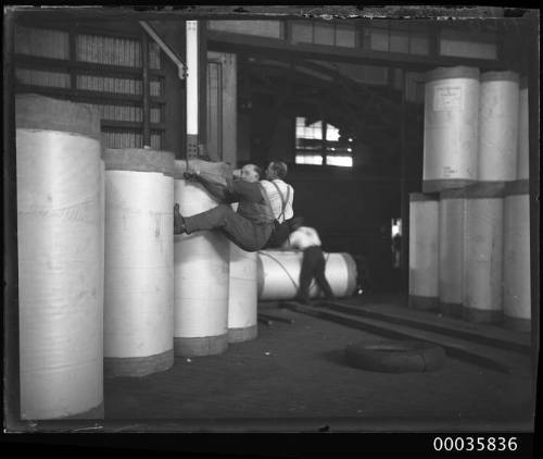 Interior view of warehouse showing workmen positioning newsprint rolls