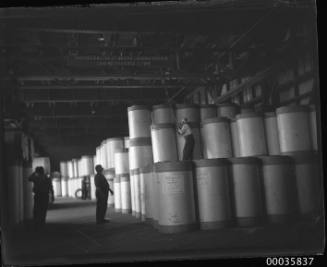 Interior view of warehouse showing workmen positioning newsprint rolls