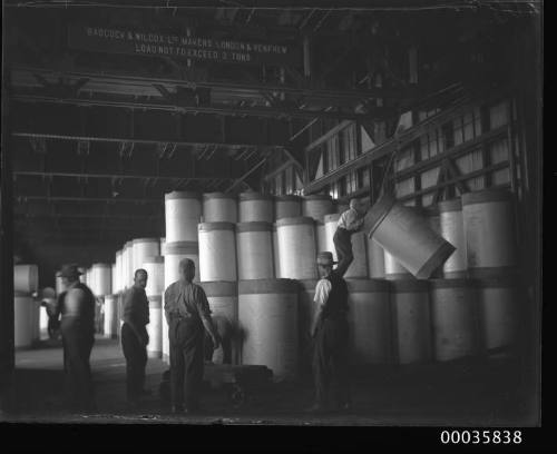 Interior view of warehouse showing workmen positioning newsprint rolls