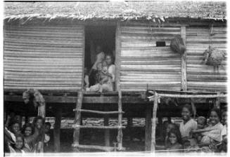 View of women and children in front of a stilted hut