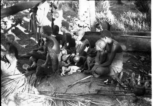 View of adults and children seated on a mat 