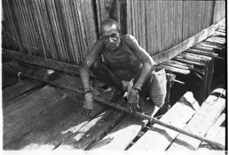 View of a man crouching by partially visible bamboo hut