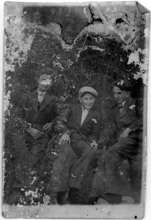 Three young men in suits sitting on grass