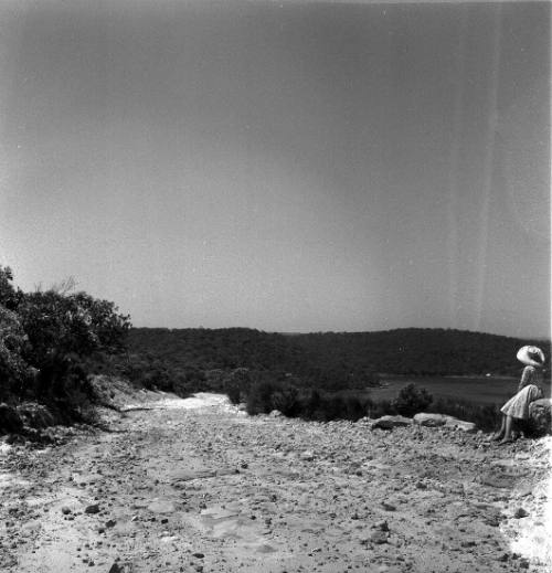 View of a woman seated on the side of a dirt road 