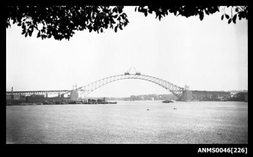 View across open water to Sydney Harbour Bridge under construction