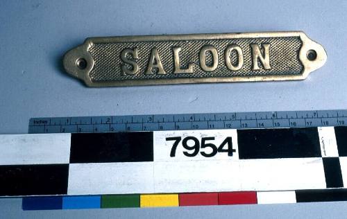 Brass metal sign with inscription reading 'SALOON'.