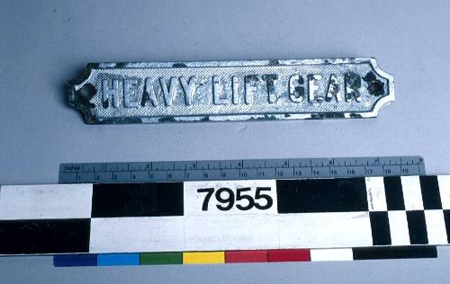 Brass metal sign with inscription reading 'HEAVY LIFT GEAR'.