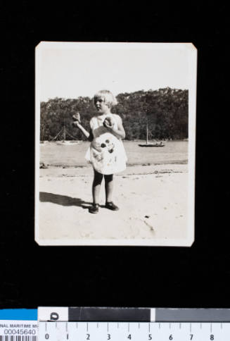 Photograph of Gloria Smythe, aged 4 years, standing on the beach at The Basin, Pittwater, holding shells