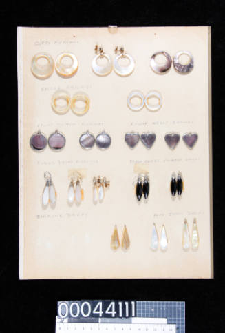 An album page with seventeen pairs of pearl shell and black coral earrings, attached with double-sided tape