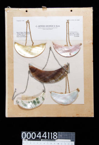 An album page with five pearl shell, crescent shaped necklaces, attached with string and tape