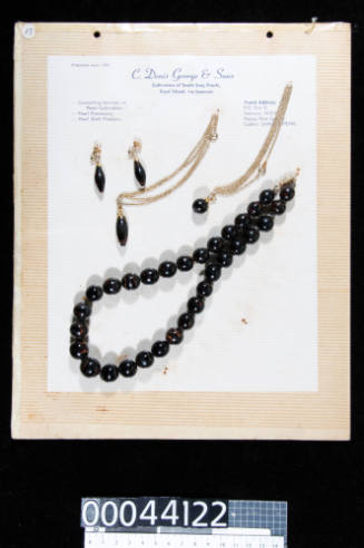 An album page with four pieces of black coral jewellery, consisting on earrings, pendants and a necklace, attached with string




