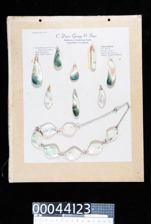 An album page with eight pendants and a necklace, made from green snail shell, attached with string and double sided tape




