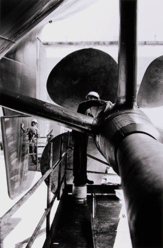 An engineer re-greases components in the propellor shaft after refitting of the propellor as another seals plugs in the rudder.