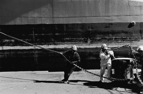 Dock workers assist the dock-master Brad Lovegrove in keeping the vessel centred as it enters the flooded dock with the assistance of winches and harbour tugs.