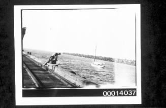 Man looking over the edge of a wooden wharf with tracks, breakwater in the distance