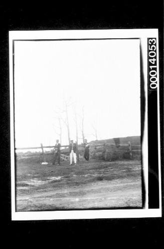 Three men standing beside a wooden fence