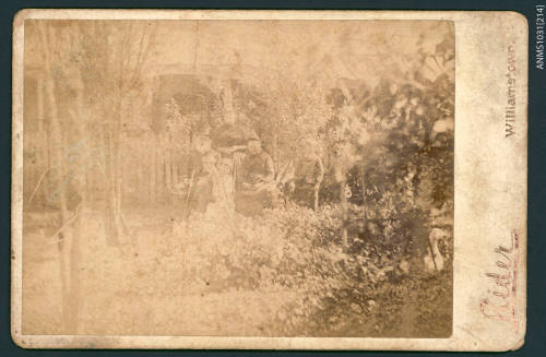 Black and white photograph of two elderly women and a man, with a small child, sitting and standing in a group in a garden