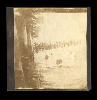 Black and white photograph of three people swimming in the water beside a wooden pier