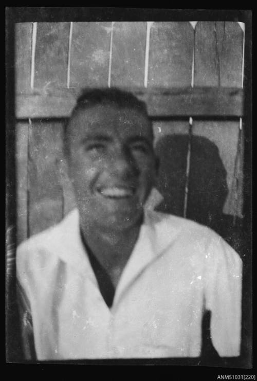 Negative of a man with a light coloured top, standing in front of a wooden fence