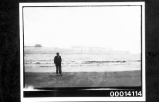 Double exposed negative with view of building in fields superimposed with an image of a man standing on the shore