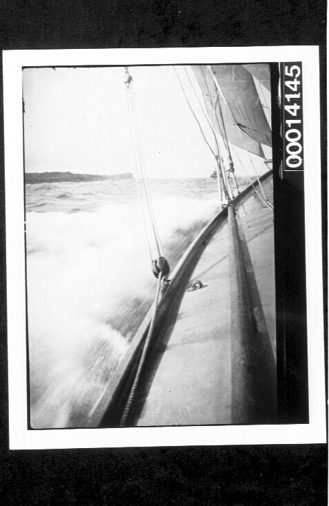 Port side of yacht under sail, headland in the distance