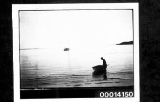 Standing next to a dinghy in shallows, yacht in the distance