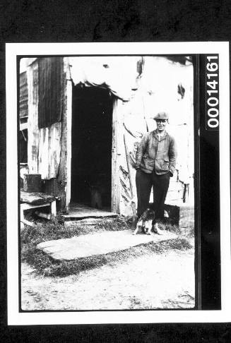 A man and his dog outside an old wooden shack