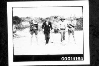 Four men standing on a beach, a shack in the distance