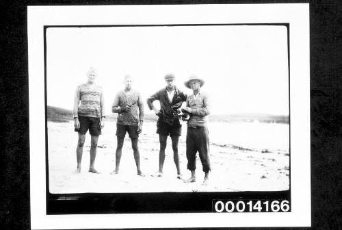 Four men standing on a beach, one holding a cat