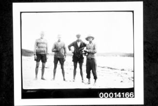 Four men standing on a beach, one holding a cat