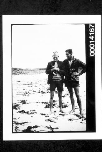 Two men standing on a beach, one holding a cat