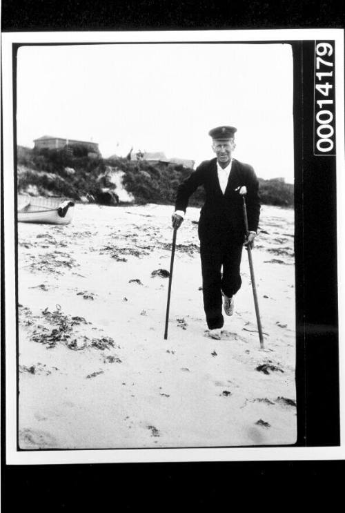 Harold Nossiter walking with a crutch and stick along a beach