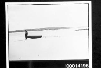 Man standing beside a dinghy on a sandy beach