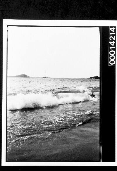 Waves breaking on the sand, a yacht moored in the distance