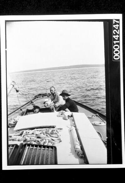 Three men in the cockpit of yacht UTIEKAH II, the coastline in the distance