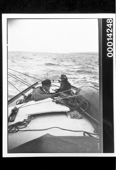 Two men in the cockpit of yacht UTIEKAH II, a promontory in the distance