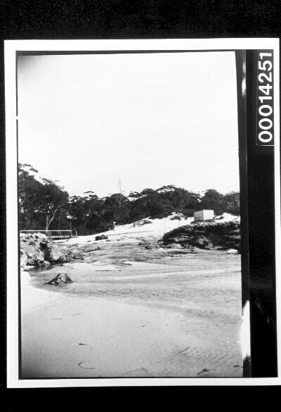 Rocks along a sandy shore, a small building in the distance